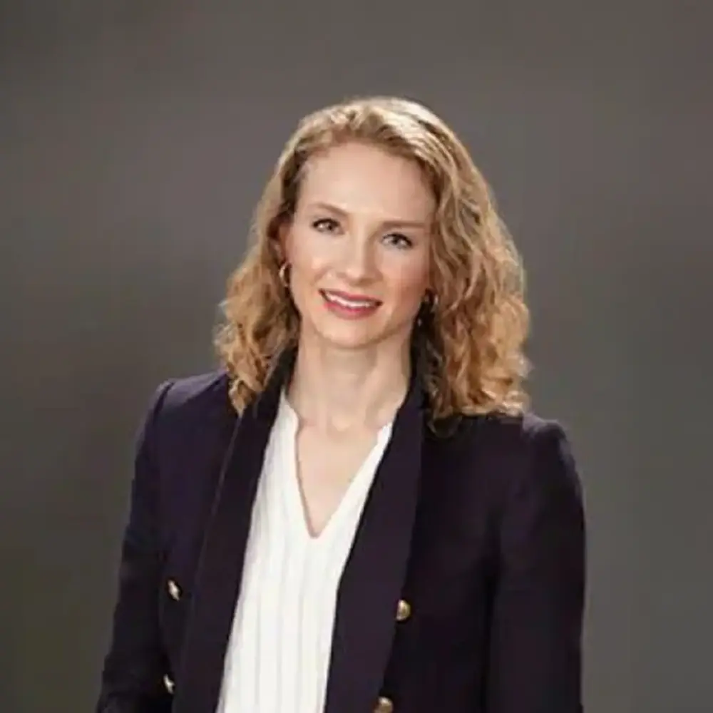 Angela Coldwell headshot, in a navy blazer against a grey backdrop