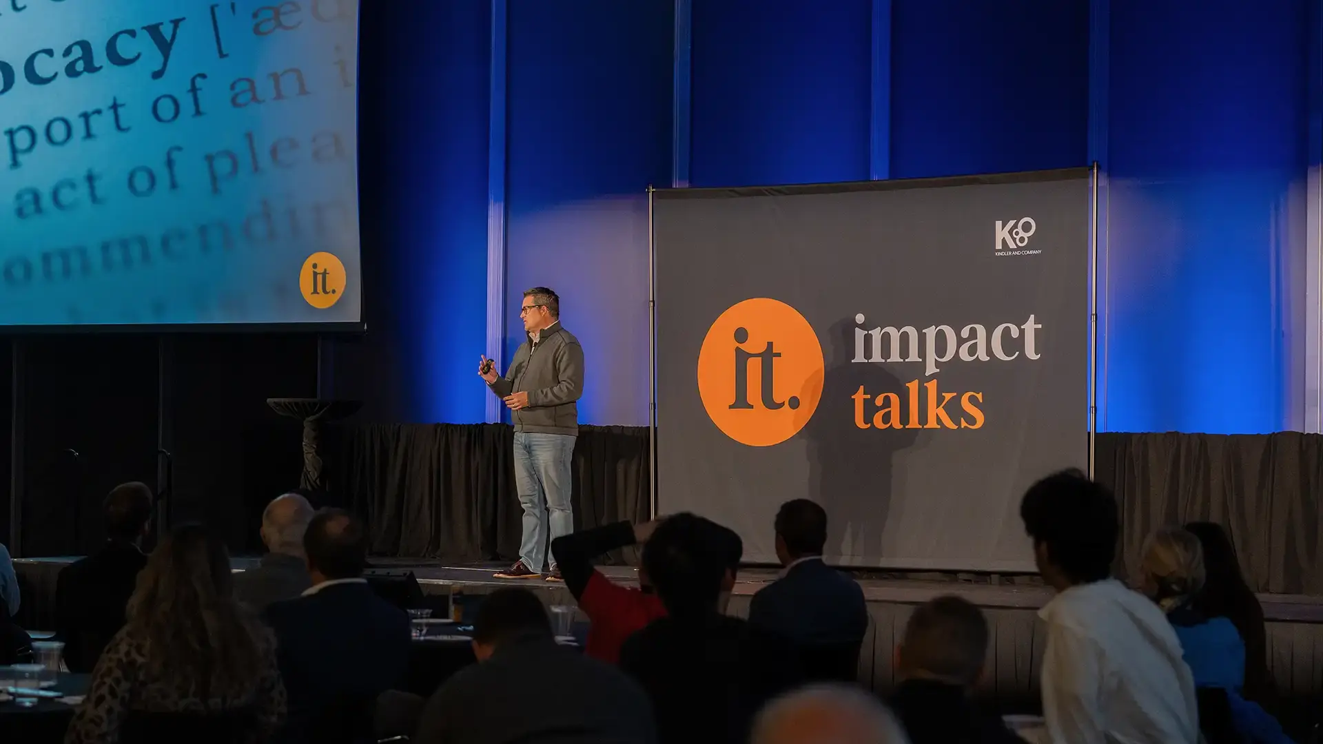 Speaker on a conference stage in front of an Impact Talks banner and seated audience