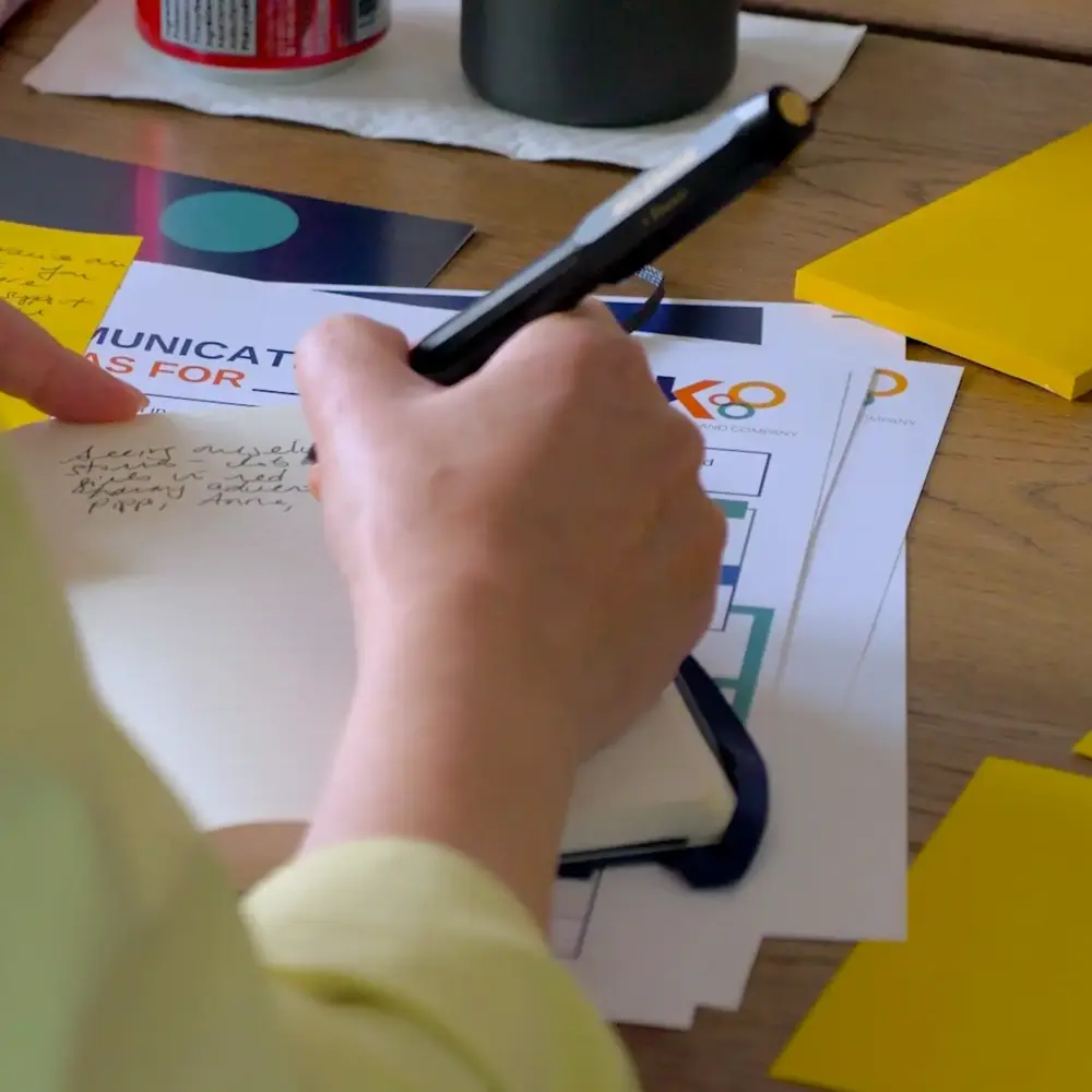 Close-up of a hand writing notes beside a Kindler worksheet and sticky notes