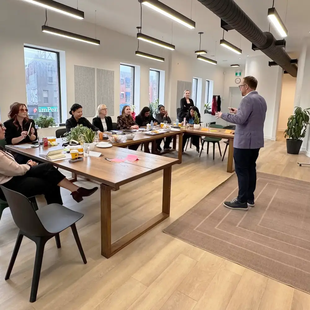 Facilitator standing before a leadership team seated around a long table in a bright Toronto workshop space
