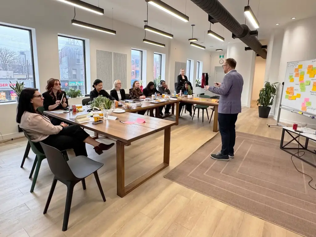Facilitator standing before a leadership team seated around a long table in a bright Toronto workshop space