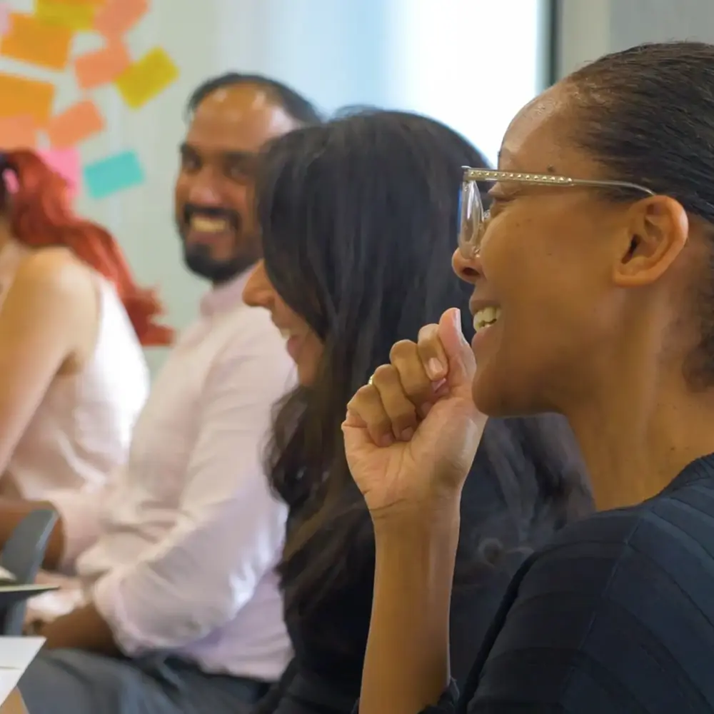 Workshop participants laughing at a table in front of a sticky-note wall