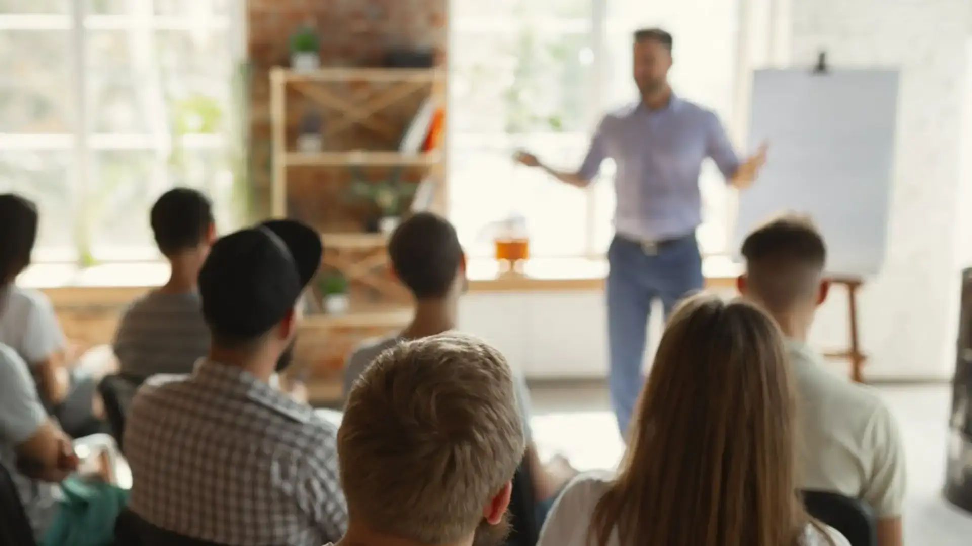 Man presenting to a seated audience in a bright, brick-walled workshop space.