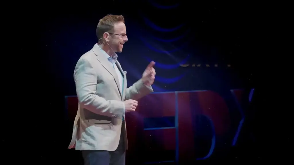 Nick Kindler speaking on a TEDx stage, mid-gesture