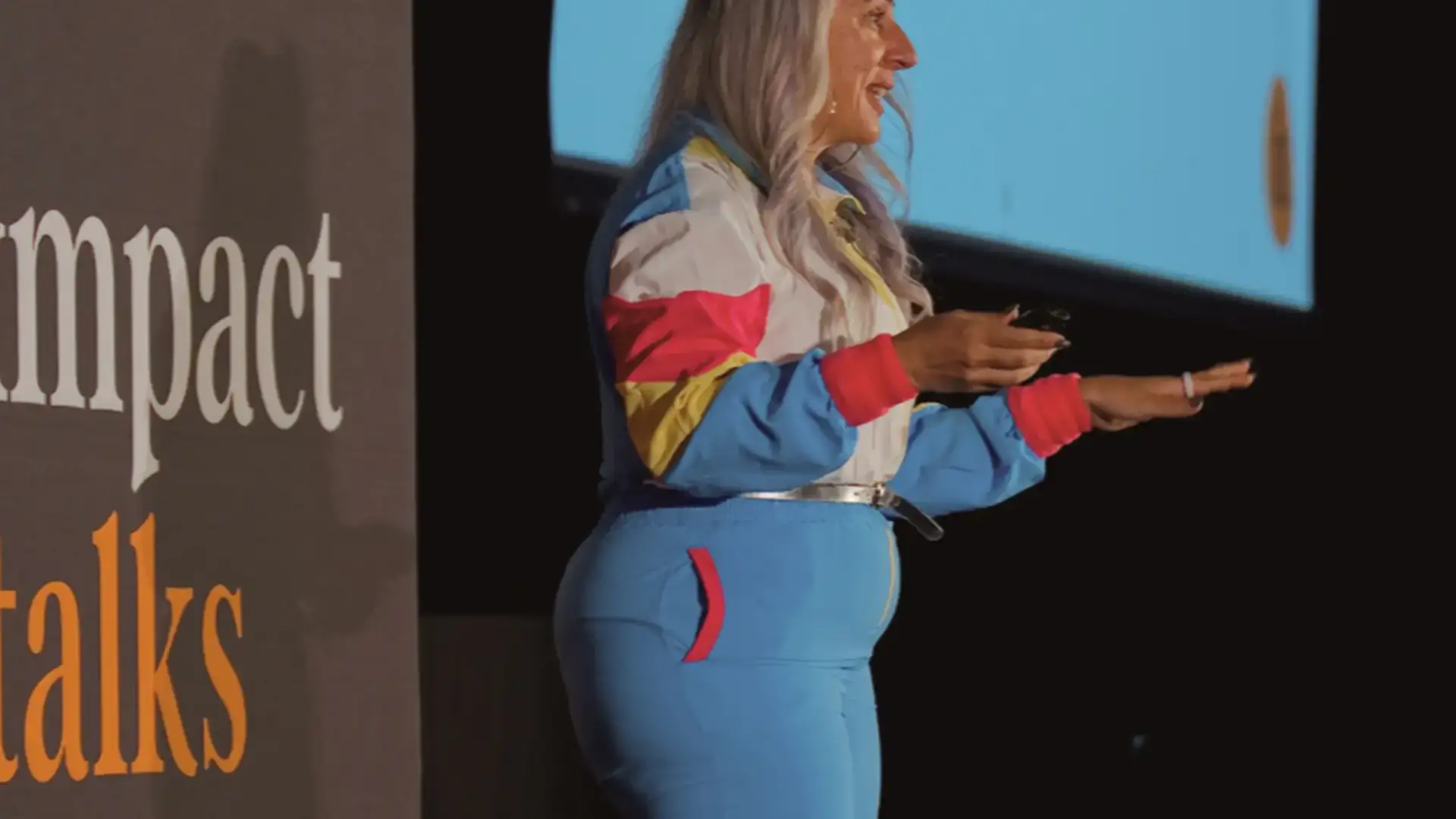 Zayna Khayat speaking onstage at Impact Talks in a colourful 1980s-style tracksuit and headband.